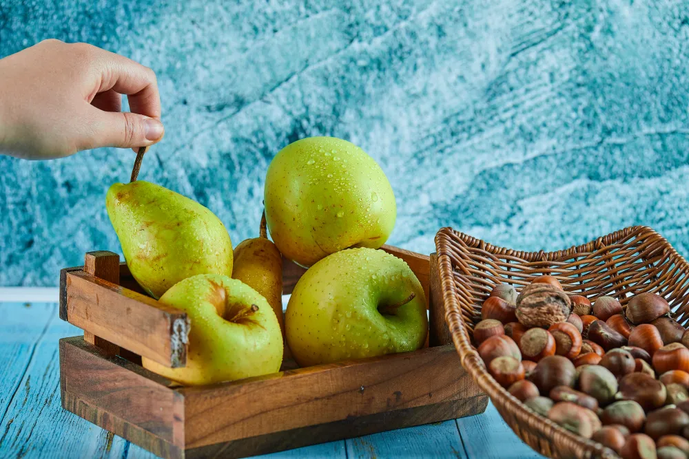 Äpfel und Birne im Korb neben einer Schale Haselnüsse