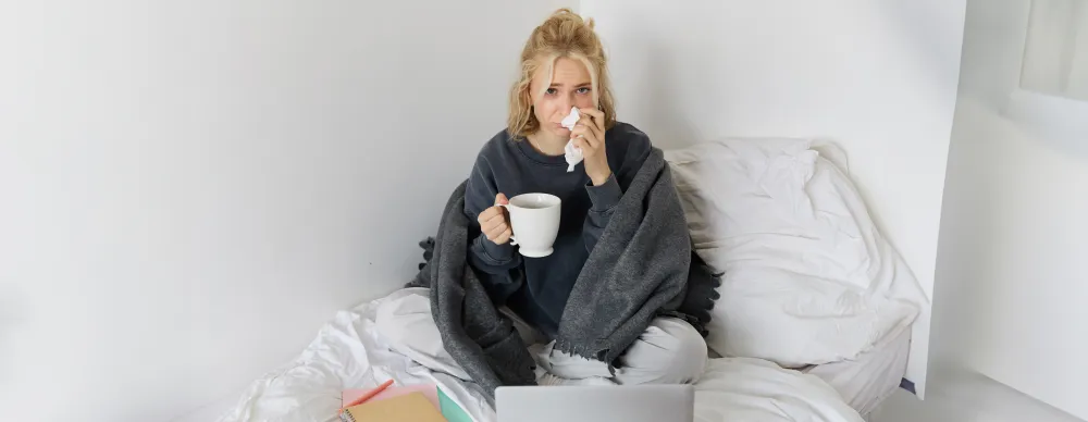 Erkältete Frau sitzt mit einer Tasse Tee im Bett